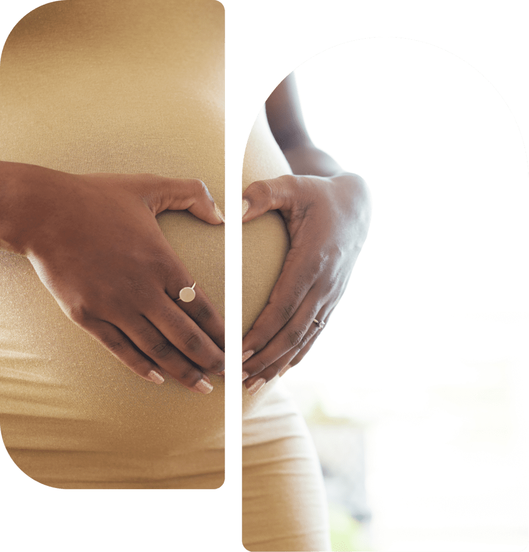 Pregnant person in a beige dress cradles their belly with both hands.