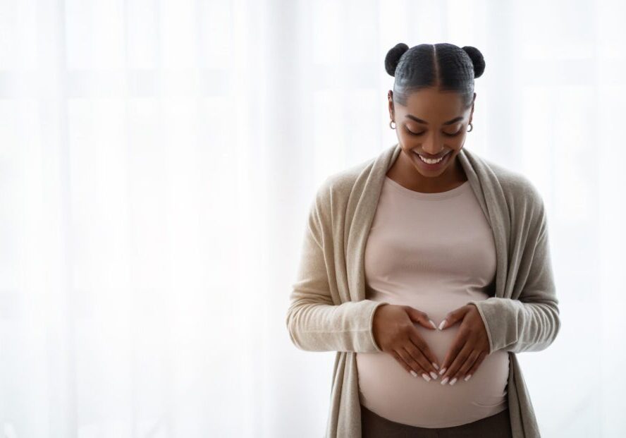 Smiling young black pregnant woman holding hands on big belly